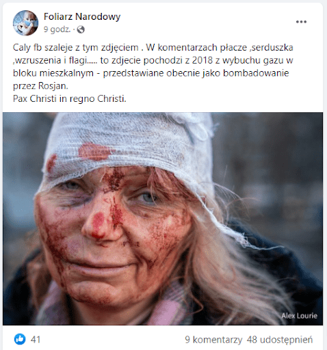 Zrzut ekranu omawianego posta na Facebooku. Na dołączonym do niego zdjęciu widzimy portret dojrzałej kobiety z wyraźnymi zmarszczkami o jasnych włosach, która ma na twarzy plamy krwi. Zmęczonym wzrokiem patrzy prosto w obiektyw. Na głowie ma bandaż, który zachodzi jej na prawe oko. Tło jest rozmazane.