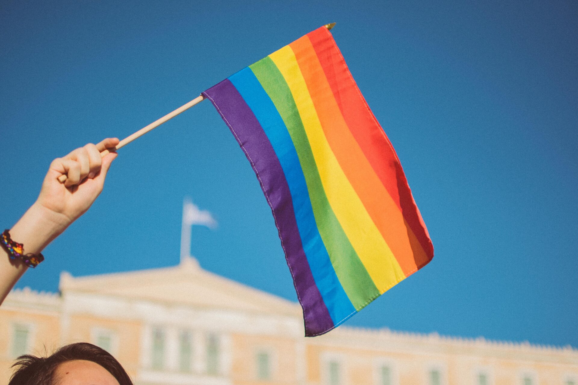 ręka trzymajaca flagę LGBT na tle zabytkowego budynku i bezchmurnego nieba