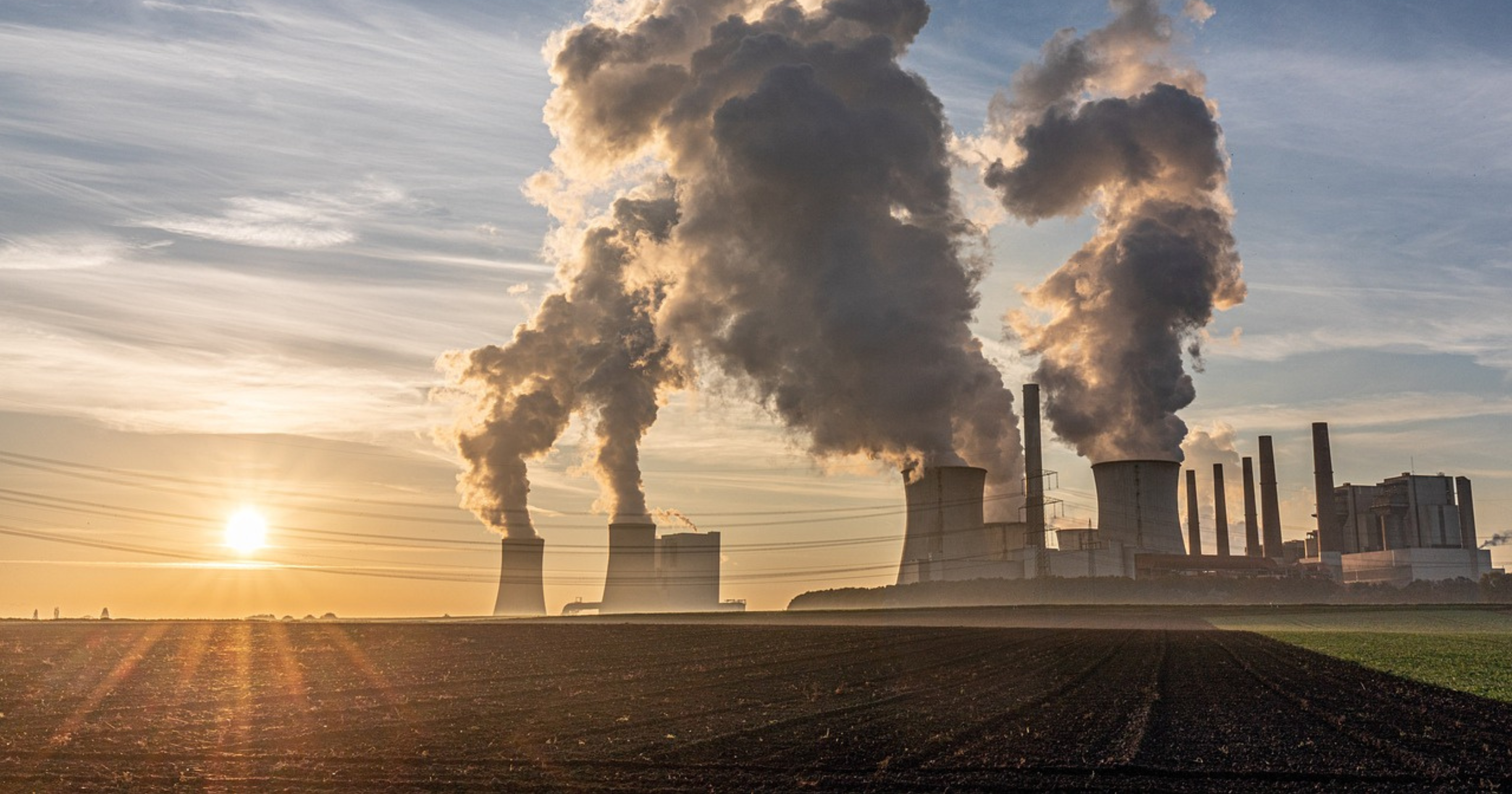 Elektrownia, nad którą unoszą się kłęby dymu na tle zachodu słońca.