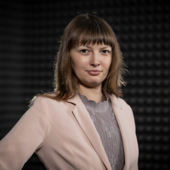 Monika Lewkowicz od klatki piersiowej w górę z ręką na boku na ciemnym tle