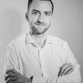 Bartosz Dybała w białej koszuli stojący z założonymi rękami