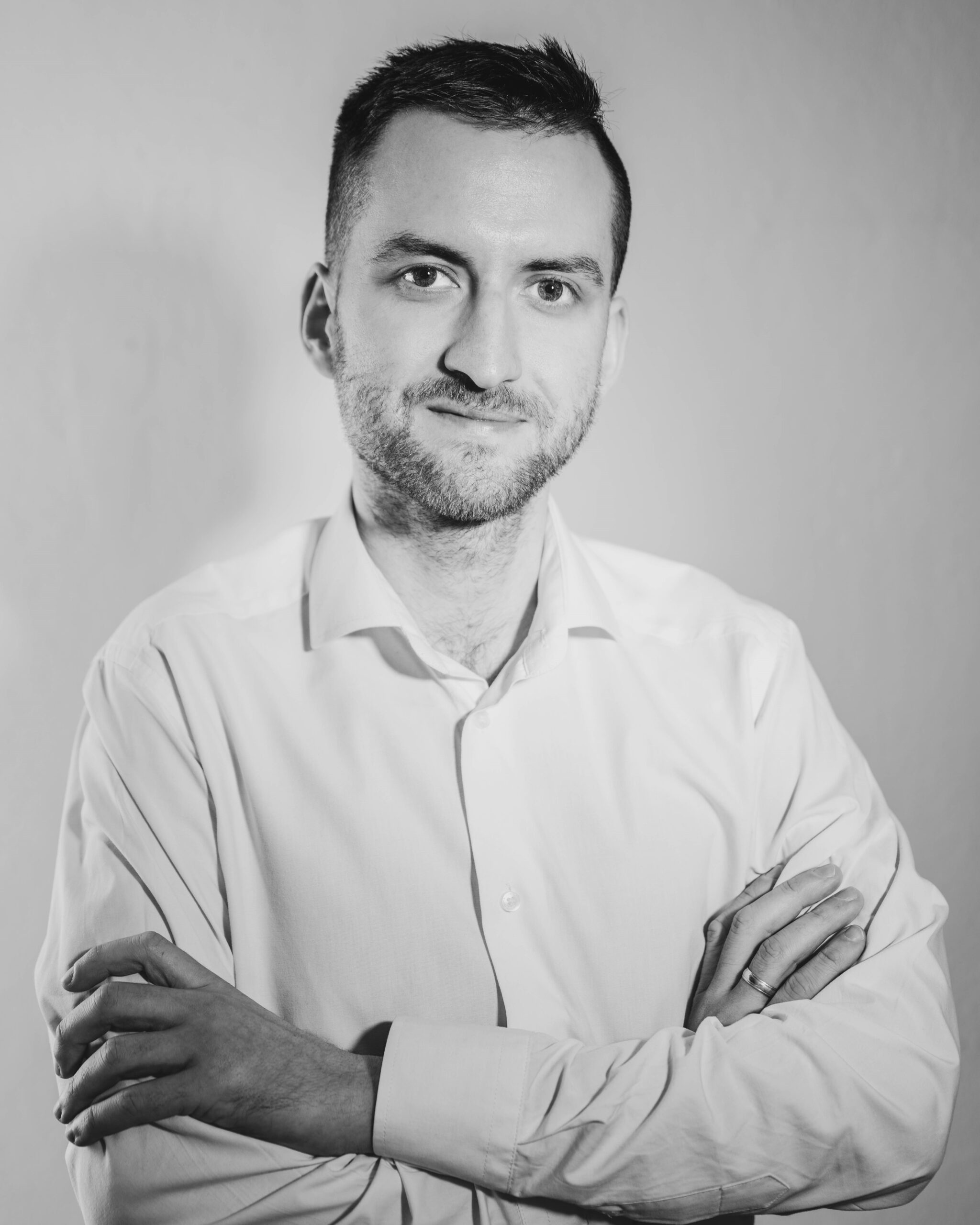 Bartosz Dybała w białej koszuli stojący z założonymi rękami