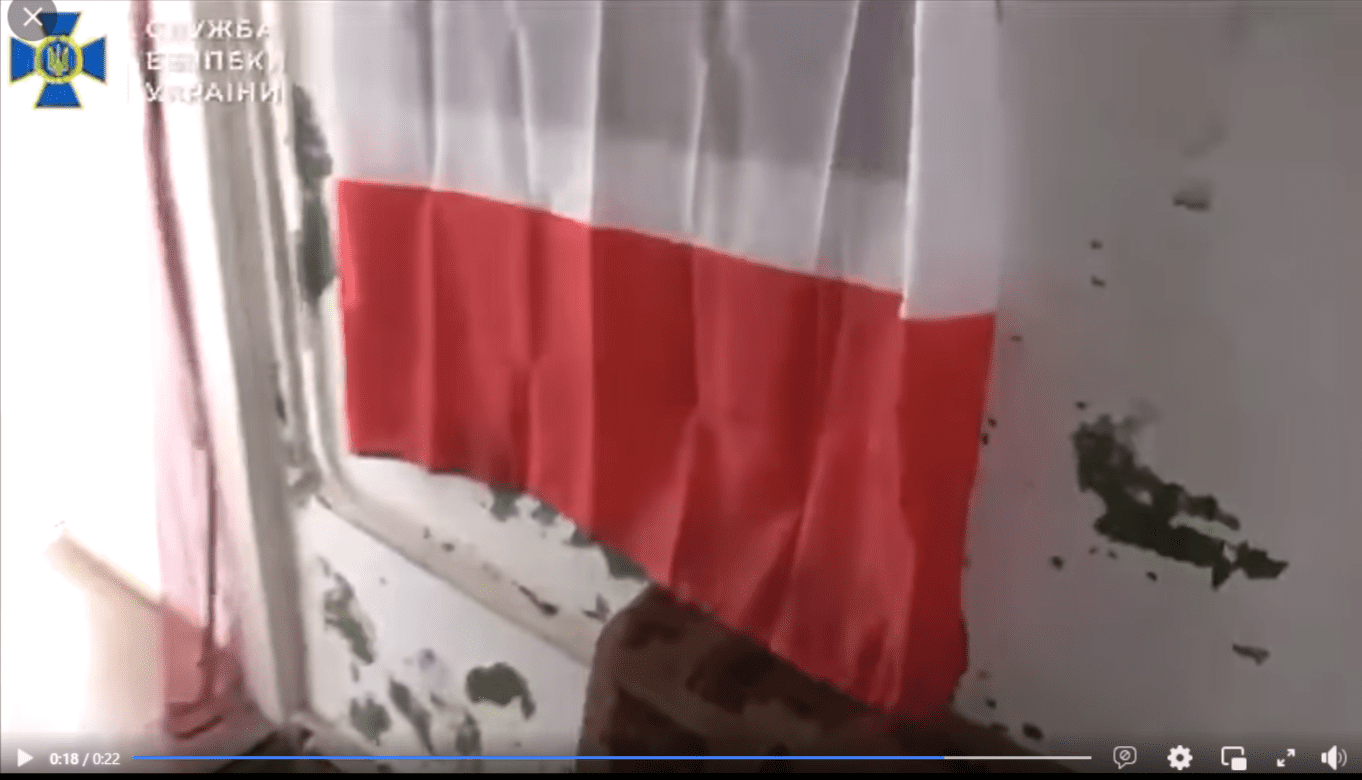 Zrzut ekranu z nagrania, w którym przedstawiono zatrzymanie grupy mężczyzn. Na stopklatce widać niedbale powieszoną polską flagę na oknie przy zadrapanej ścianie.